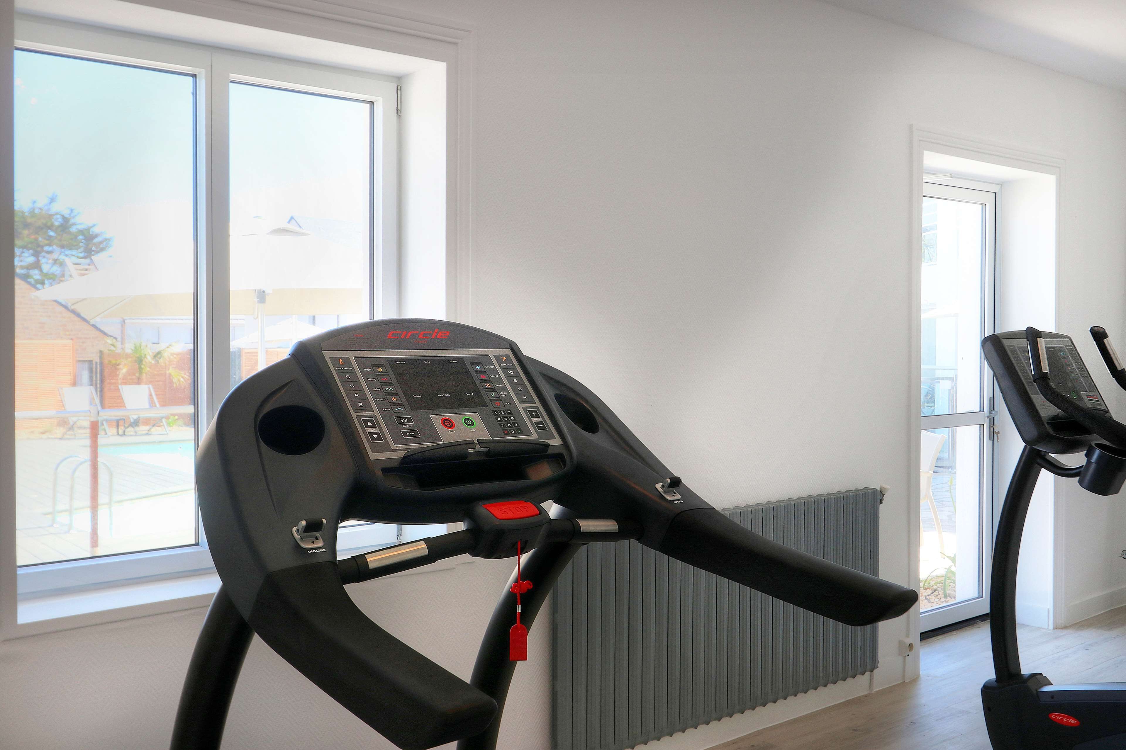 A treadmill in a room with large windows, a radiator, and a door leading outside.