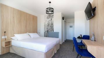 Ein Hotelzimmer mit Bett, Schreibtisch mit Stühlen, einem an der Wand befestigten Fernseher und einem Wandradiator.
