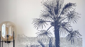 A room with a blue sofa, a wall mural of palm trees, and a floor lamp. - Best Western Hotel Le Bellevue (Quiberon)