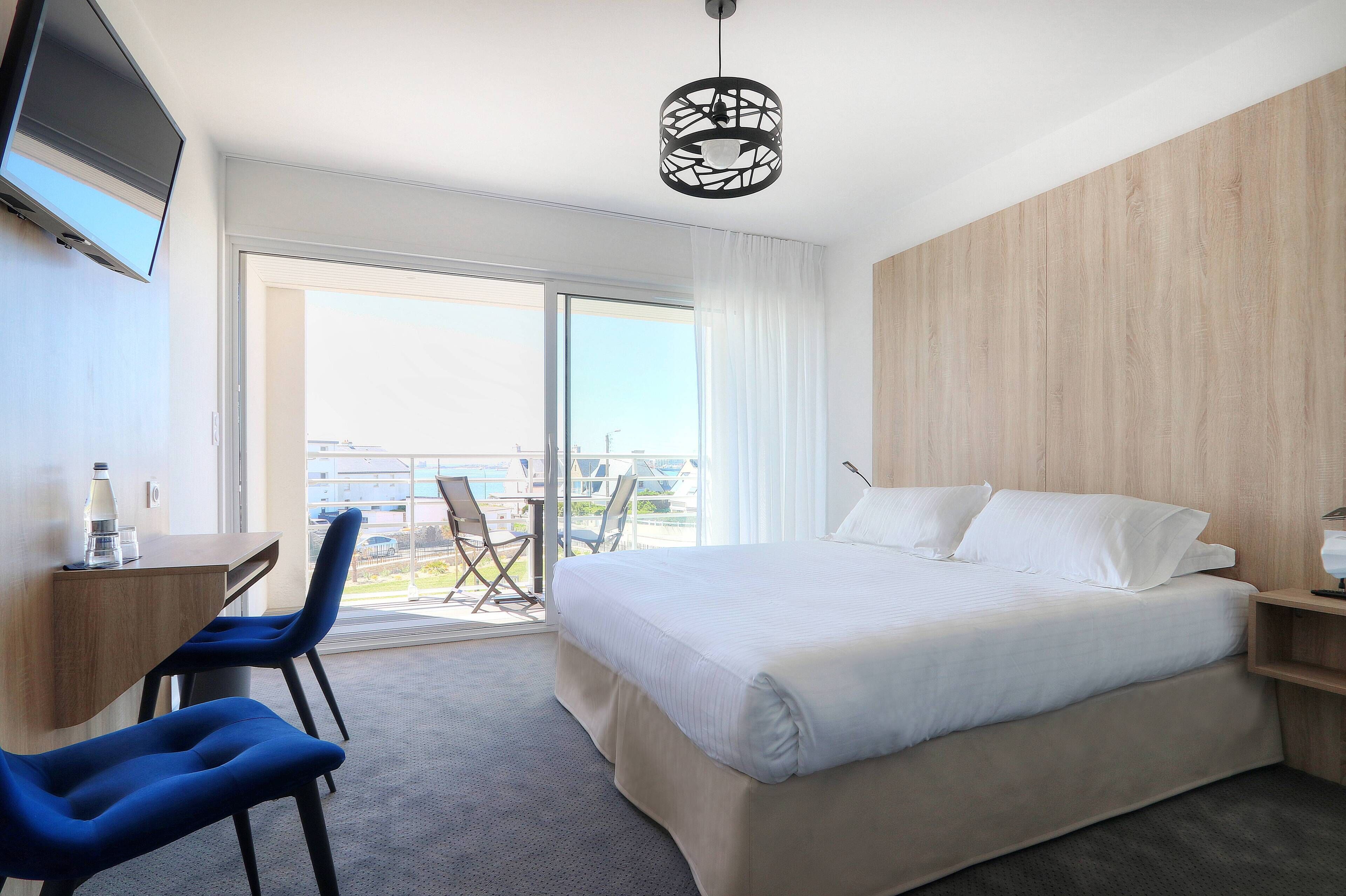 Une chambre d’hôtel équipée d’un lit, d’un bureau, de deux chaises, d’une télévision et offrant une vue sur l’extérieur.