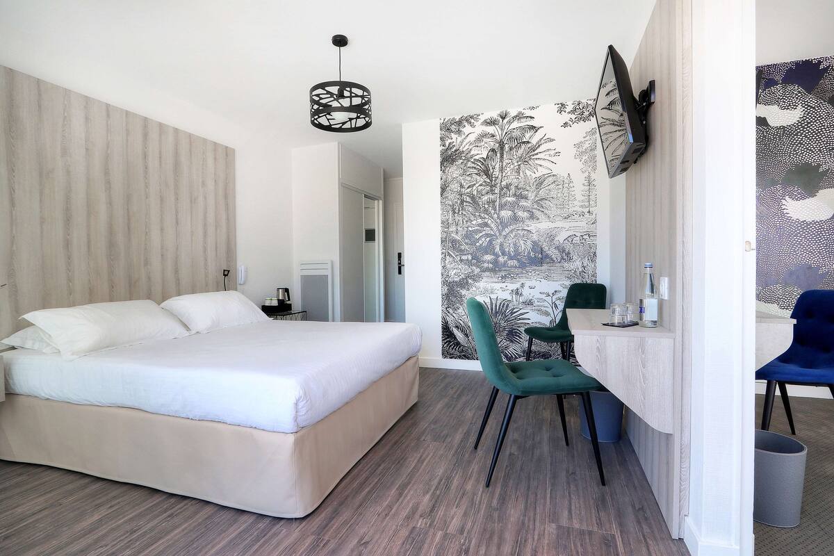 Quarto moderno com uma cama grande, uma escrivaninha com cadeiras, uma TV fixada na parede e um papel de parede estampado.
