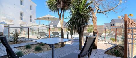 An outdoor patio with a table and chairs, surrounded by palm trees and a pool area.