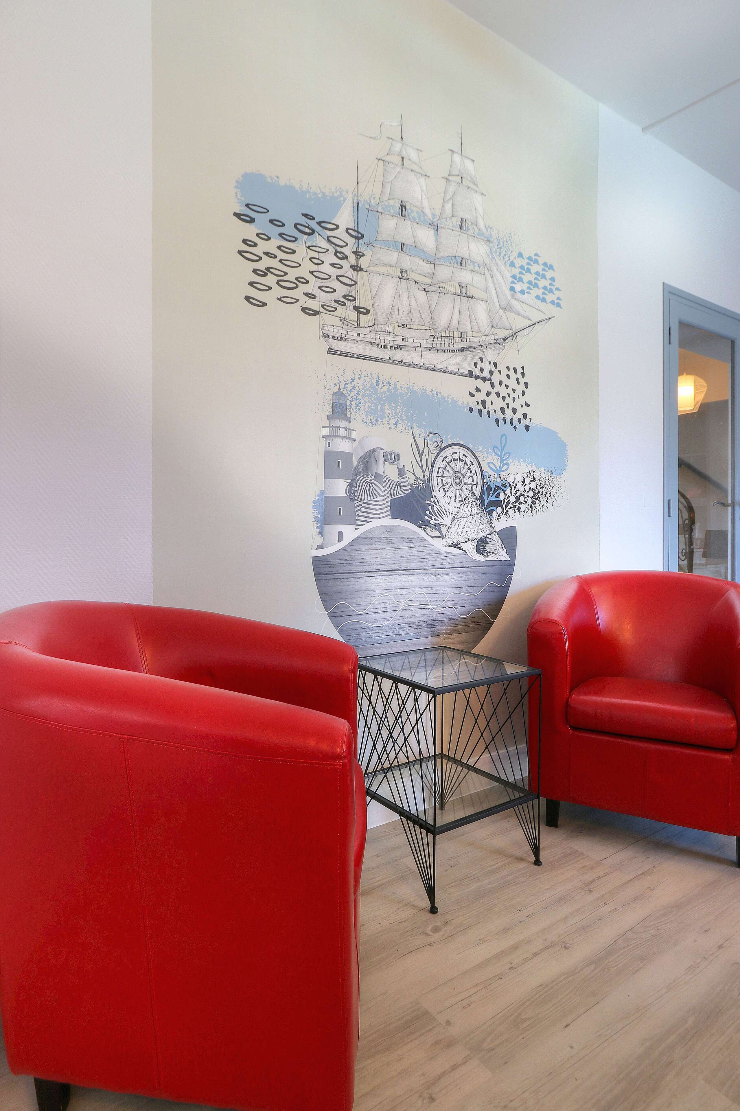 Ein Zimmer mit zwei roten Stühlen, einem Glastisch und einem Wandbild mit einem Schiff und einem Leuchtturm.