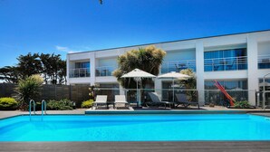 A modern hotel with a swimming pool, outdoor seating, and a clear blue sky. - Best Western Hotel Le Bellevue (Quiberon)