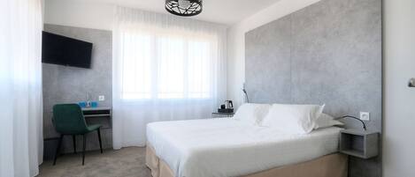 A modern hotel room with a large bed, a desk with a chair, a flat-screen TV, and a pendant light.