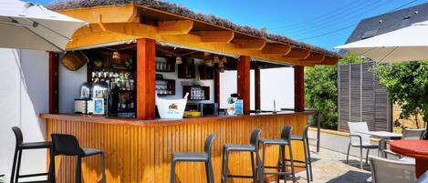Un área de bar al aire libre con mobiliario de madera y techo de paja.