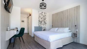 Una habitación de hotel moderna con una cama, un escritorio con una silla, un televisor y una lámpara fijada a la pared.
