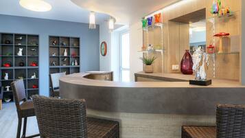 A modern reception area with a curved counter, wicker chairs, and shelves with decorative items.