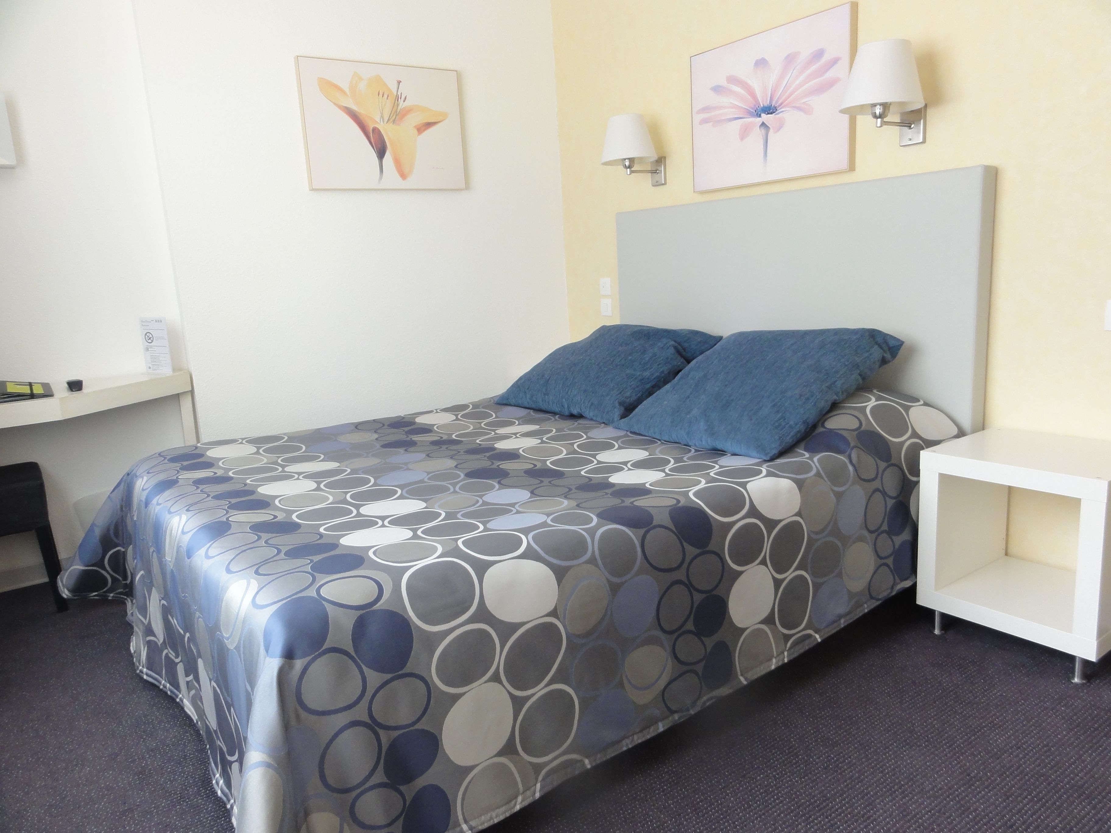 A neatly arranged hotel room with a bed, two pillows, a bedside table, and a desk.