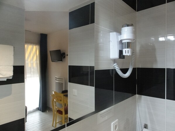 Un baño con baldosas blanco y negro, un cabezal de ducha blanco, una silla de madera y un televisor montado en la pared.