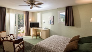 A hotel room with a bed, desk, chair, television, and a balcony with curtains. - Hôtel Princess (Vernet-les-Bains)