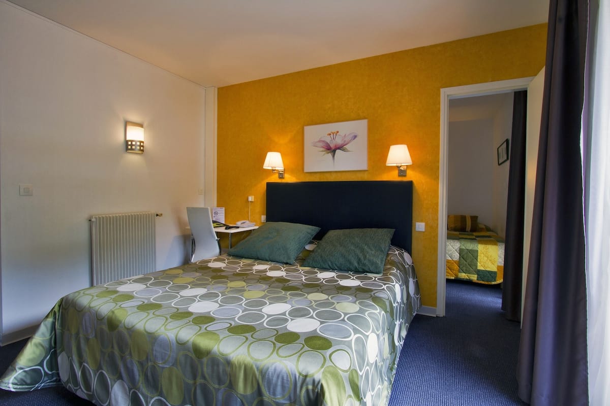 Ein Hotelzimmer mit einem Bett, zwei Nachttischlampen, einer Heizung und einer Tür zu einem anderen Raum.