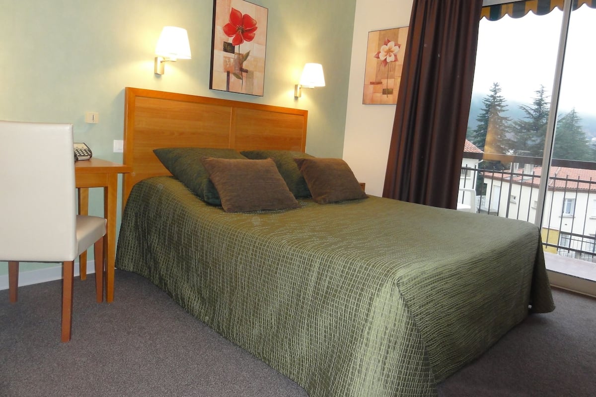 Ein Hotelzimmer mit einem Bett, zwei Kissen, einem Sessel, einem Schreibtisch mit Telefon und zwei Wandlampen.