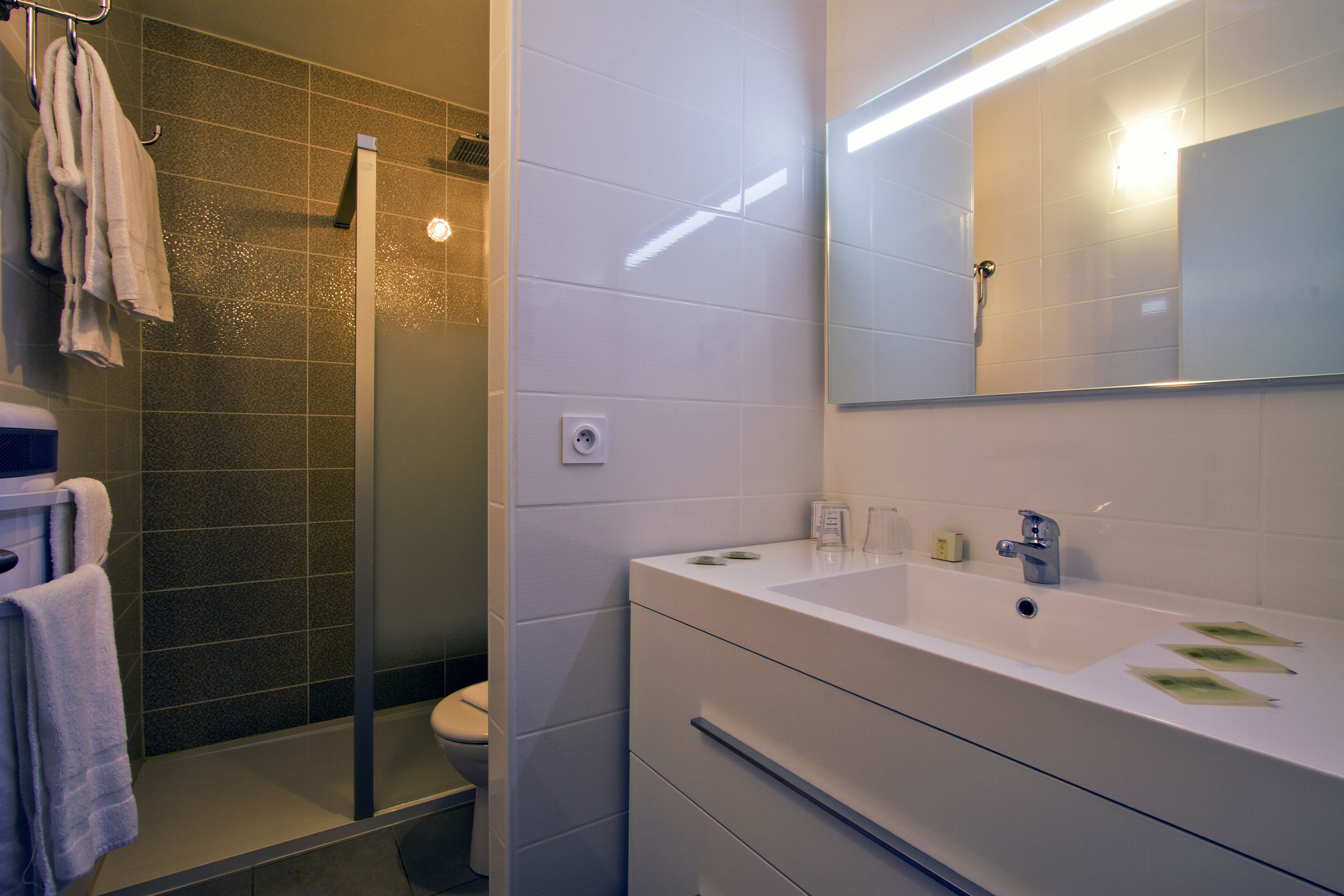 Un baño moderno con ducha envuelta en vidrio, un lavamanos blanco con espejo arriba y un inodoro.