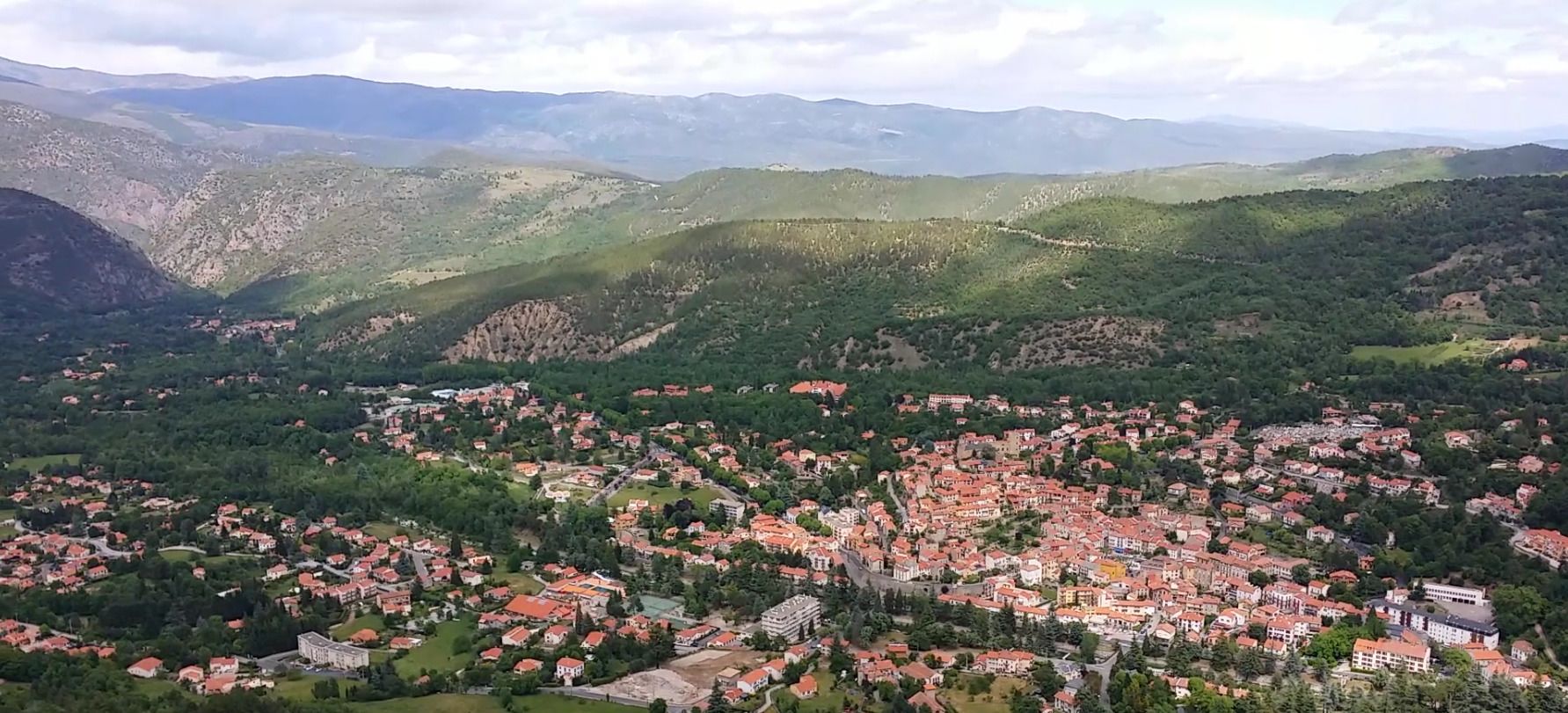 A town nestled in a valley with red-roofed buildings and green hills in the background.