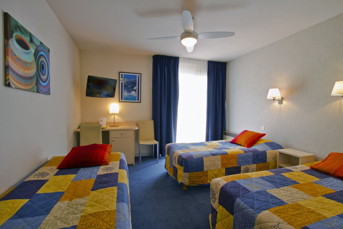 Ein Hotelzimmer mit zwei Betten, einem Schreibtisch, einem Stuhl, einem Fernseher und einem Deckenventilator.