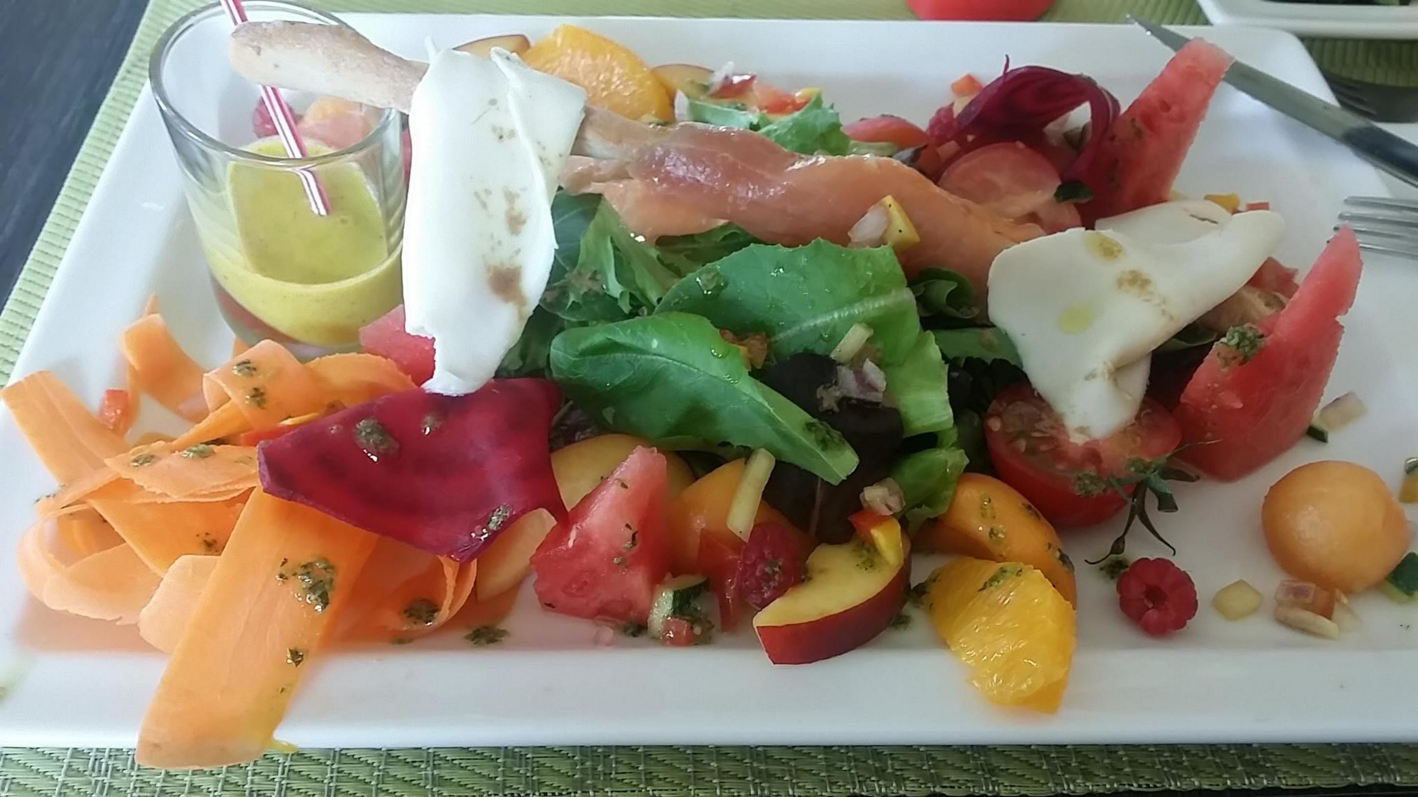 A plate of mixed salad with various vegetables and a glass of yellow drink.