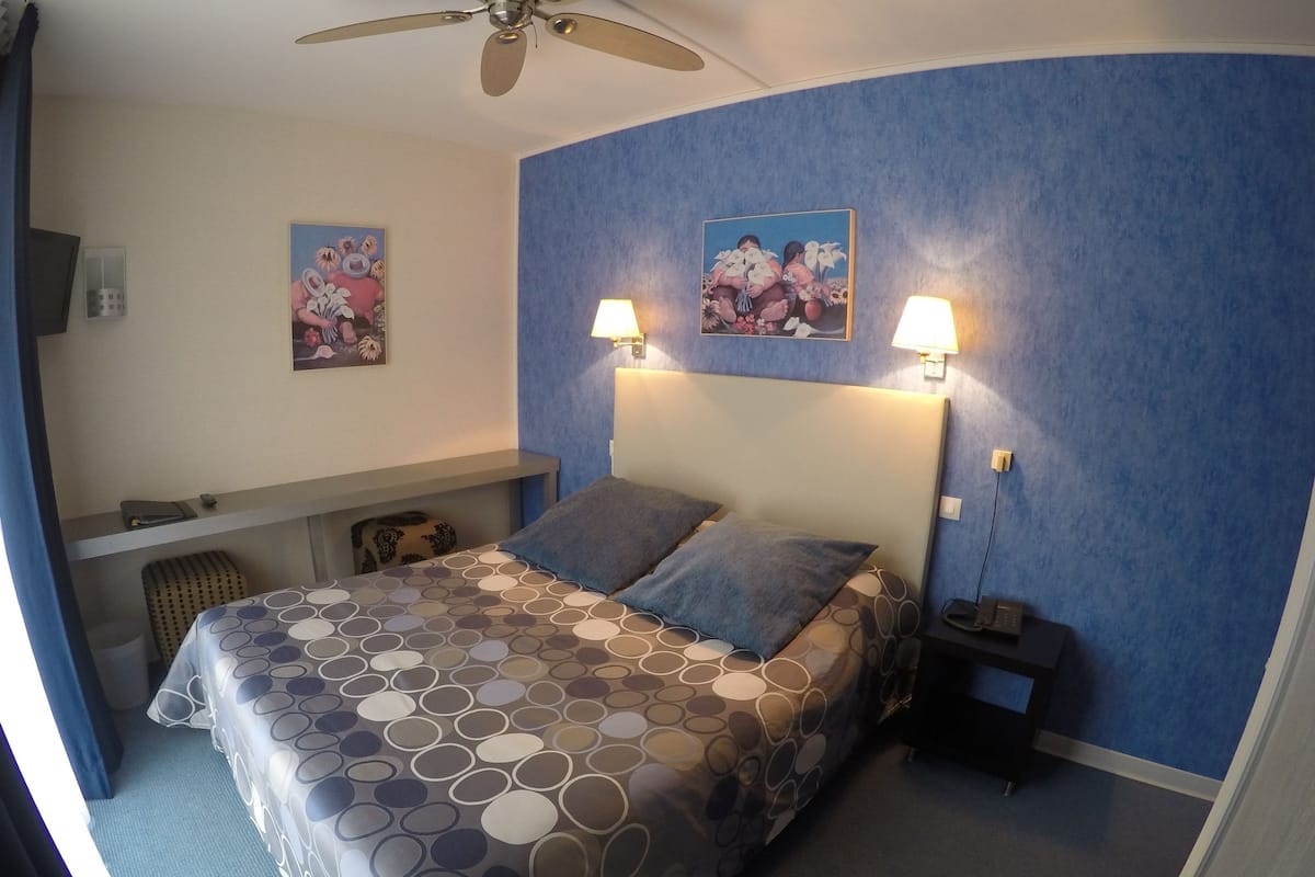 Ein Hotelzimmer mit einem Bett, zwei Wandlampen, einem Deckenventilator und zwei Bildern.