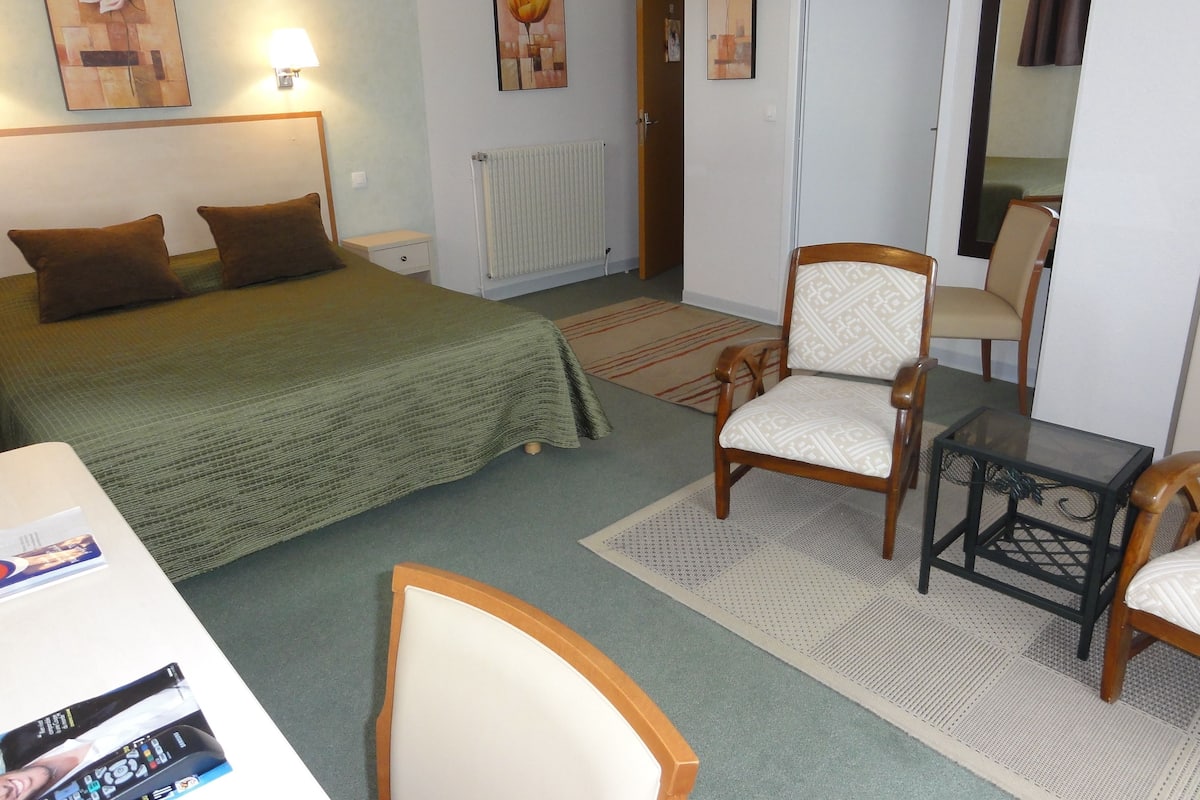Ein Hotelzimmer mit einem Bett, zwei Stühlen, einem kleinen Tisch und Bildern an den Wänden.