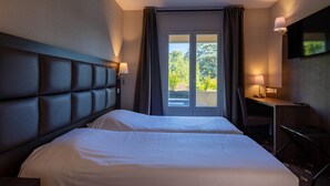 A hotel room with a large bed, a desk with a chair, a TV mounted on the wall, and a window with curtains. -  Logis Hotel Noemys Morgon (Villie-Morgon)
