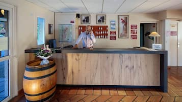 Ein Empfangsschalter mit Holzoptik, eine Karte an der Wand und ein Schwarzes Brett mit Aushängen.