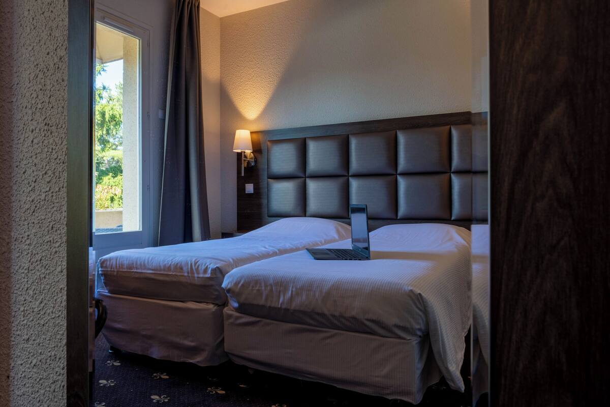 A hotel room with two beds, a laptop on one bed, and a lamp on the nightstand.