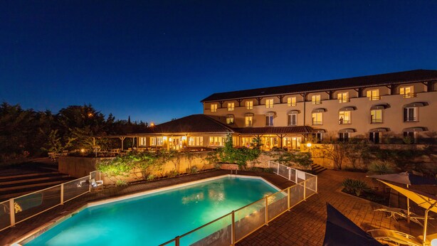 A swimming pool with a glass enclosure, surrounded by a patio area with outdoor seating and a building in the background. -  Logis Hotel Noemys Morgon (Villie-Morgon)