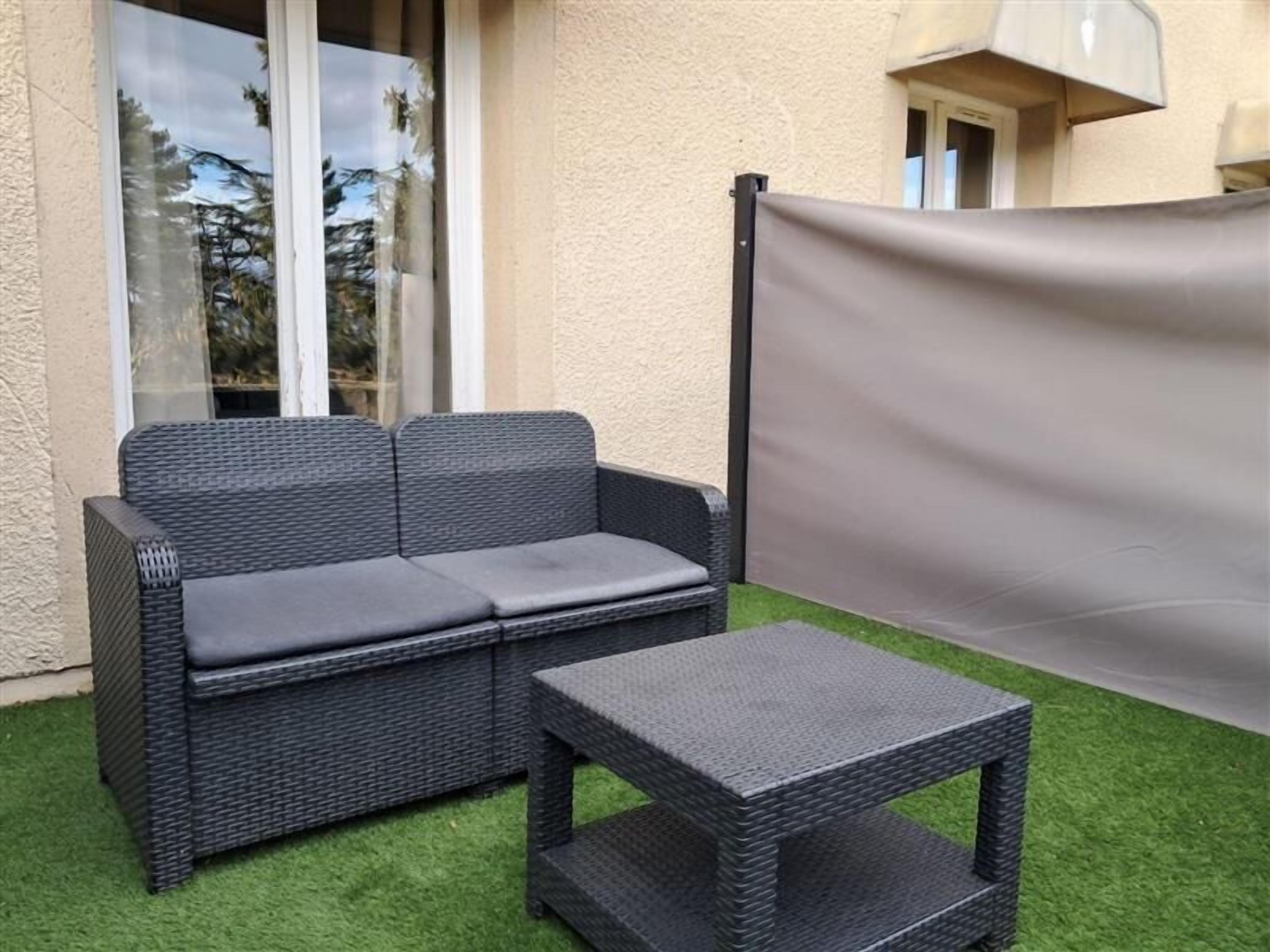 A wicker sofa and a matching table set on artificial grass, with a window and a door in the background.