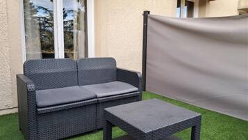 A wicker sofa and a matching table set on artificial grass, with a window and a door in the background.