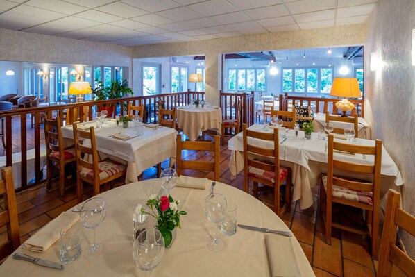 A restaurant with multiple tables, chairs, and a view of greenery through large windows.