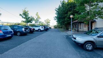 Un parking où plusieurs voitures sont garées le long d’une rue bordée d’arbres, et un bâtiment doté d’une entrée abritée.