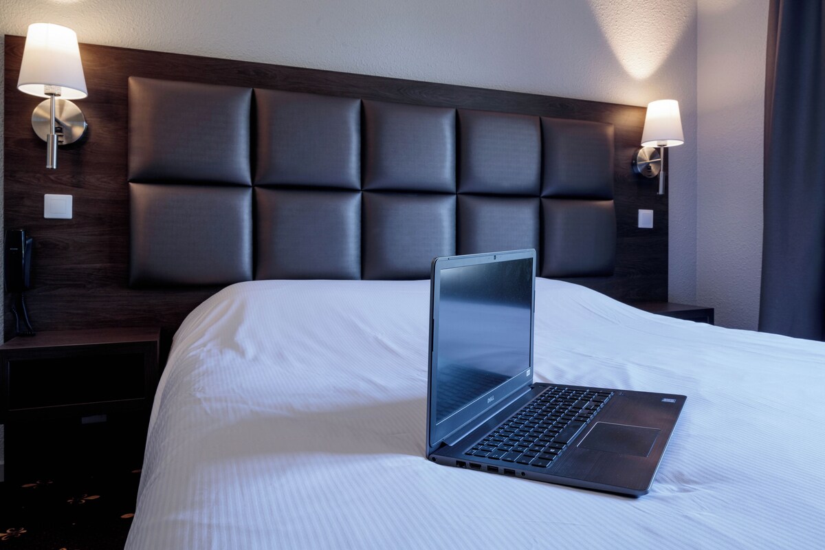 Habitación de hotel con una cama, un ordenador portátil sobre la cama y dos lámparas fijadas a la pared.