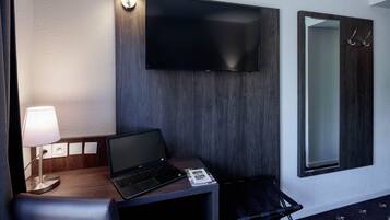 Ett hotellrum med en platt-TV som är monterad på väggen, en bärbar dator på ett skrivbord i trä, en lampa och en stol.