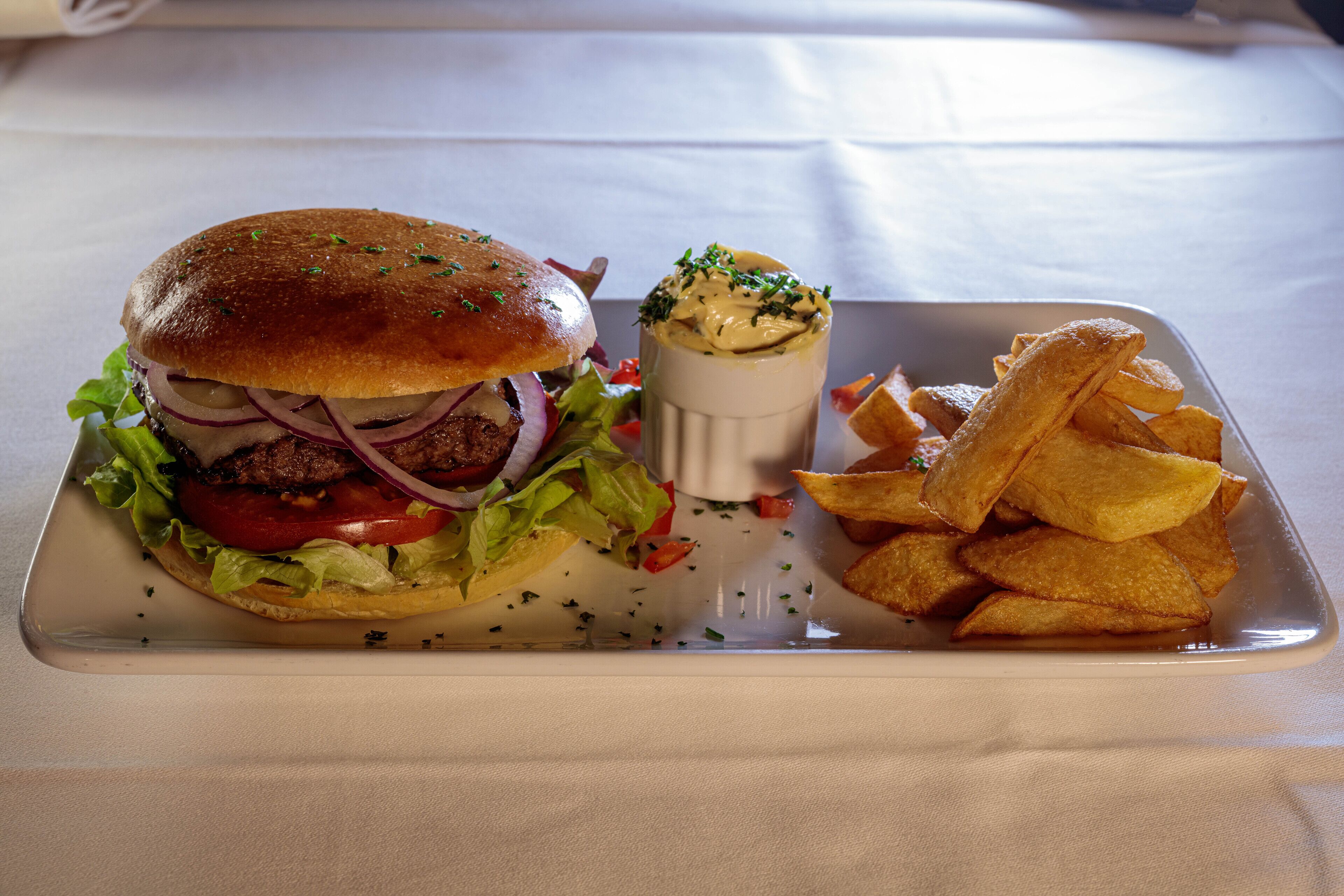 Eine Mahlzeit mit einem Burger, Pommes und einer Soße auf einer weißen Tablett.