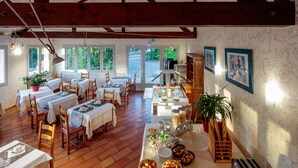 A dining area with multiple tables set for breakfast, a bread rack, a toaster, and a potted plant. -  Logis Hotel Noemys Morgon (Villie-Morgon)