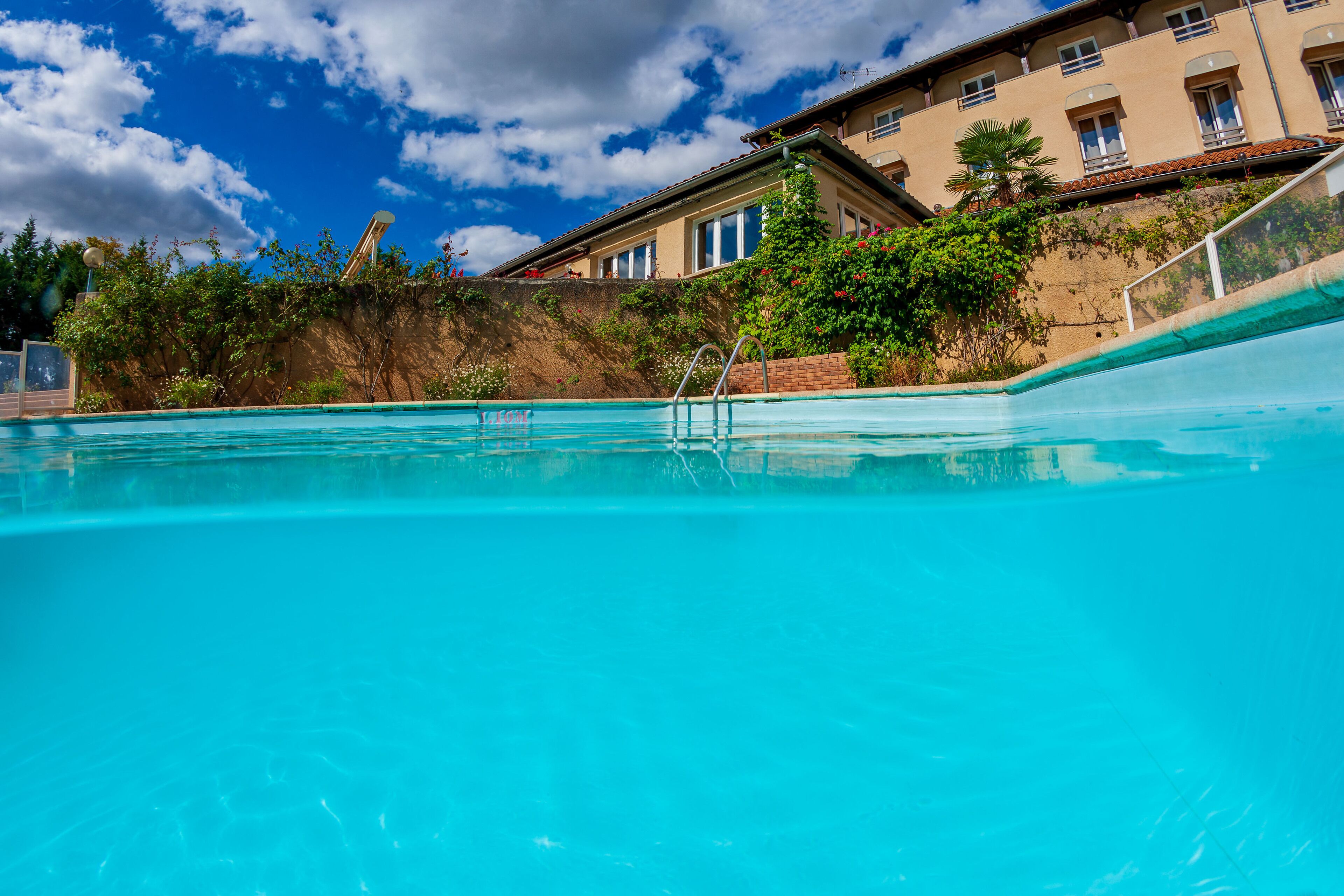 Une piscine à l’eau d’un bleu cristallin, entourée d’un bâtiment doté de nombreuses fenêtres et d’un mur en briques.