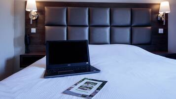 A hotel room with a bed, a laptop, and a magazine on the bed.