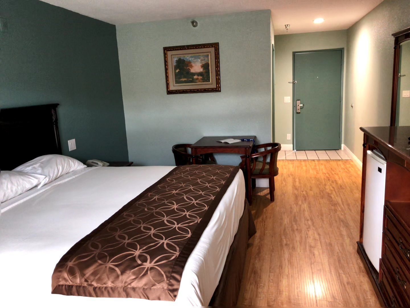 A hotel room with a bed, a desk, a chair, a dresser, and a door.
