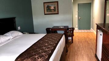 A hotel room with a bed, a desk, a chair, a dresser, and a door.