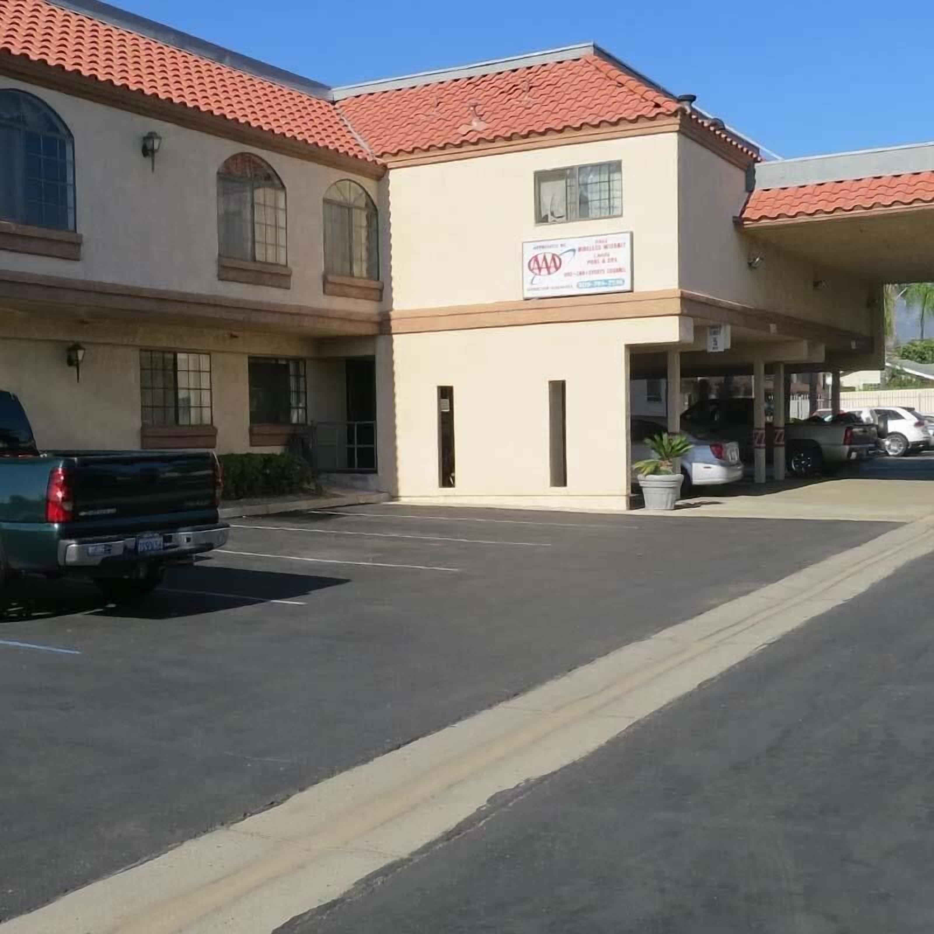 A building with a red-tiled roof, a sign indicating it is a AAA-rated hotel, and a parking lot with several vehicles.