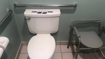 A standard toilet with a raised seat and grab bars, a white toilet paper holder, and a tiled floor.