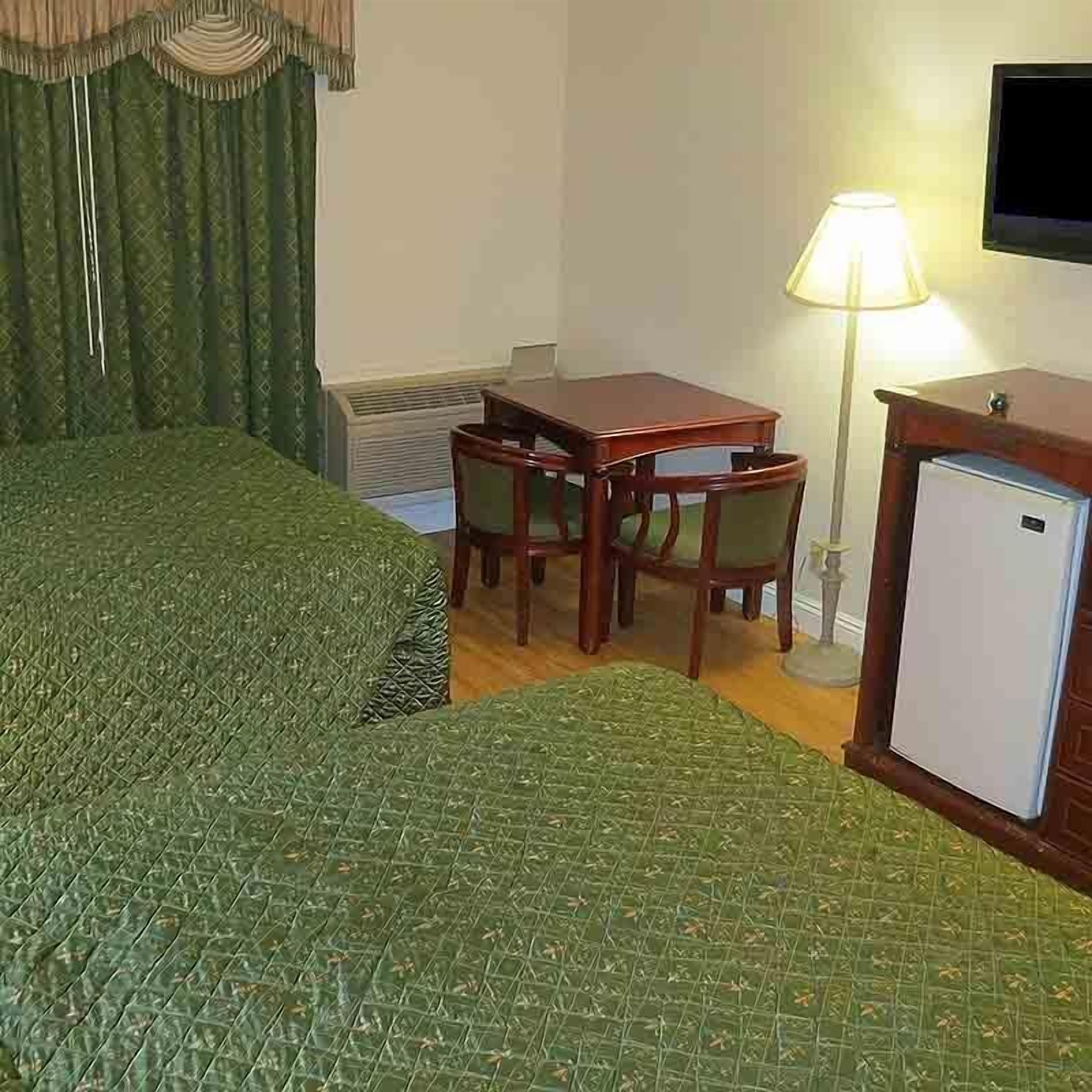 Une chambre d’hôtel comprenant un lit, un bureau avec deux chaises, une lampe et un petit réfrigérateur.