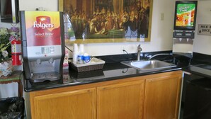Une cuisine équipée d’une machine à café, d’un évier et d’un distributeur de jus.