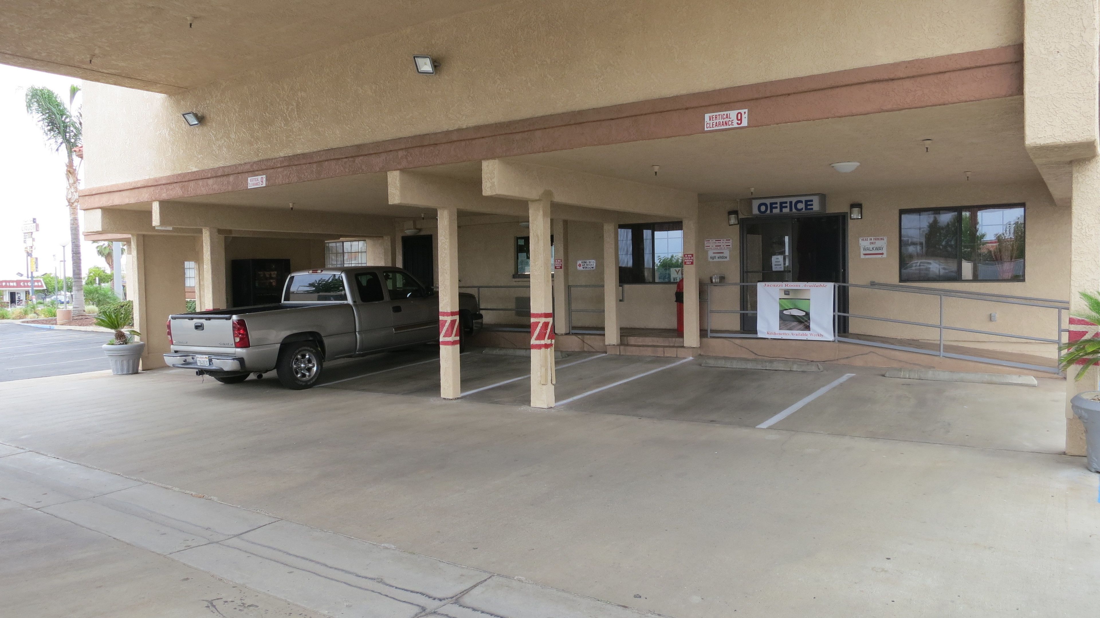 A parking garage entrance with a pickup truck parked inside, a sign indicating a 9-foot vertical clearance, and an office building with a sign that reads "OFFICE".