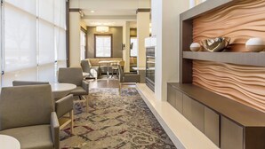 A modern hotel lobby with a seating area, a patterned carpet, and a decorative wall with a bowl and two spherical objects.