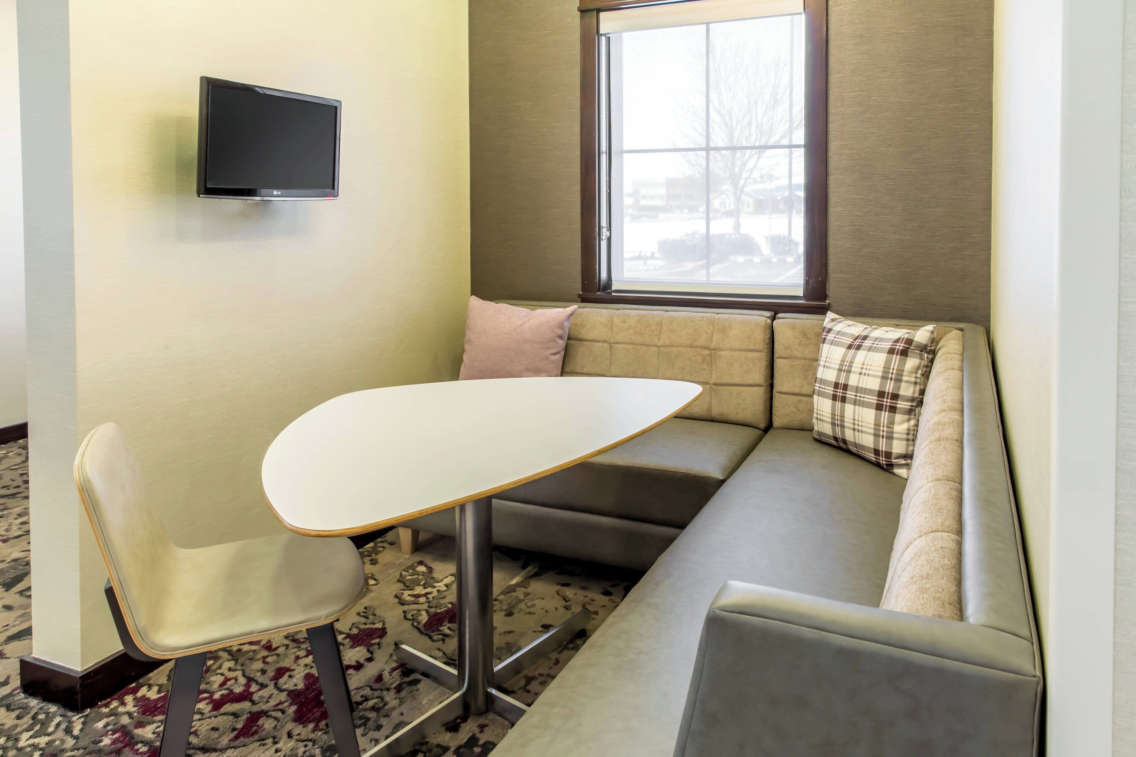 A compact room with a sofa, a small table, a chair, a flat-screen TV, and a window with a view of the outside.