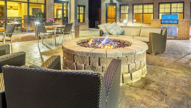 An outdoor patio area with a fire pit, wicker furniture, and a brick wall.