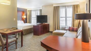 A hotel room with a bed, a TV on a wooden stand, a sofa, a desk with a chair, and a lamp.
