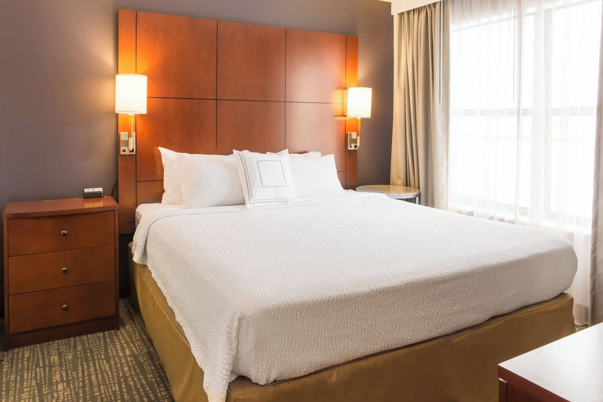 A hotel room with a large bed, two bedside tables, a wooden headboard, and two wall-mounted lamps.