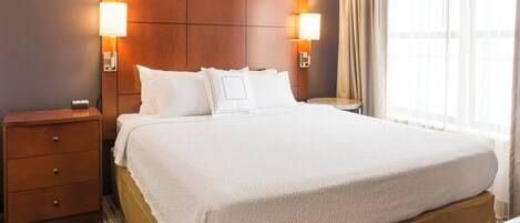 A hotel room with a large bed, two bedside tables, a wooden headboard, and two wall-mounted lamps.